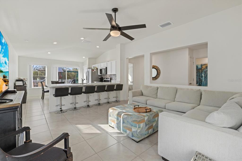 A bright open-concept living room features a large sectional sofa, kitchen island, and tile flooring — 9120 SANDY BLUFFS CIRCLE, PARRISH, FL