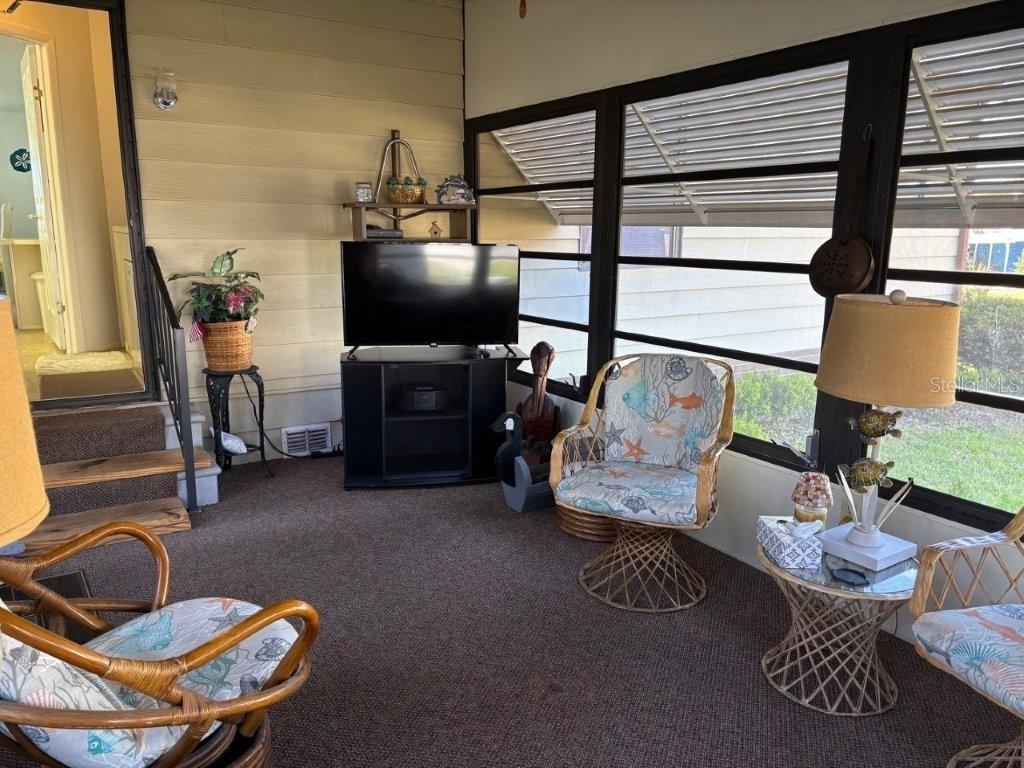 A sunroom features brown carpeting, wicker chairs with patterned cushions, a television, and large windows — 617 WEBB WAY, LADY LAKE, FL