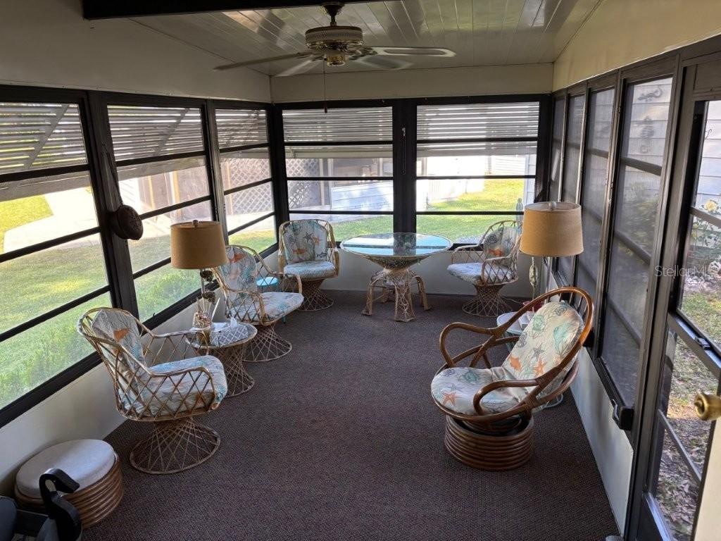 A sunroom features wicker furniture, a ceiling fan, and large windows overlooking a grassy yard — 617 WEBB WAY, LADY LAKE, FL