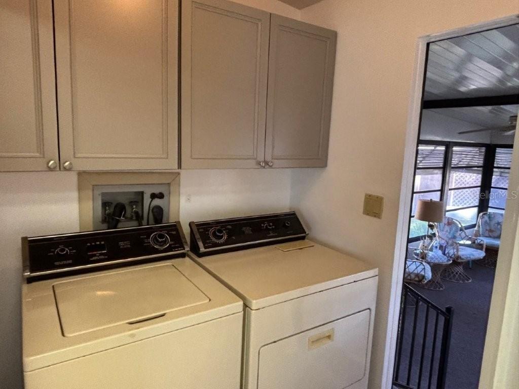 A laundry room features beige appliances, light gray cabinets, and a doorway to a sunroom — 617 WEBB WAY, LADY LAKE, FL