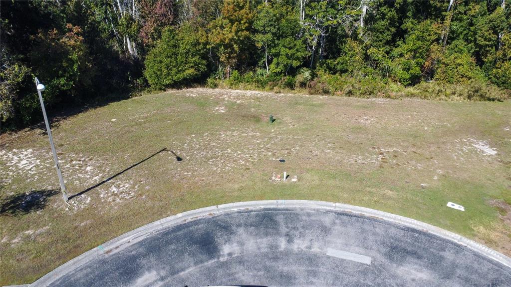 An aerial view shows a vacant, grassy residential lot situated along a curved asphalt street — 0 FOREST GLENN DRIVE, SPRING HILL, FL