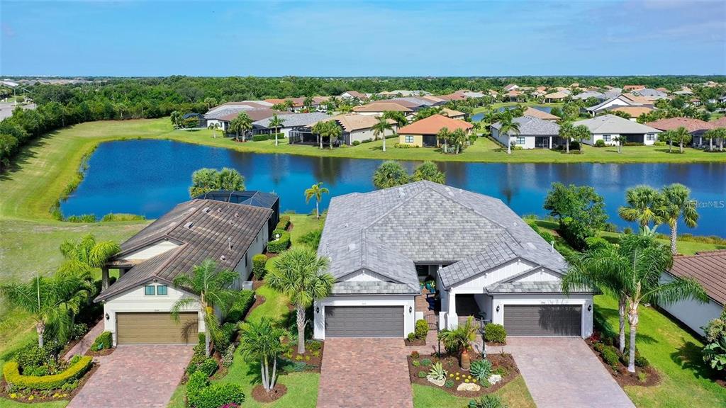An aerial view shows two suburban houses with garages and driveways beside a large pond — 7636 KIRKLAND COVE, LAKEWOOD RANCH, FL