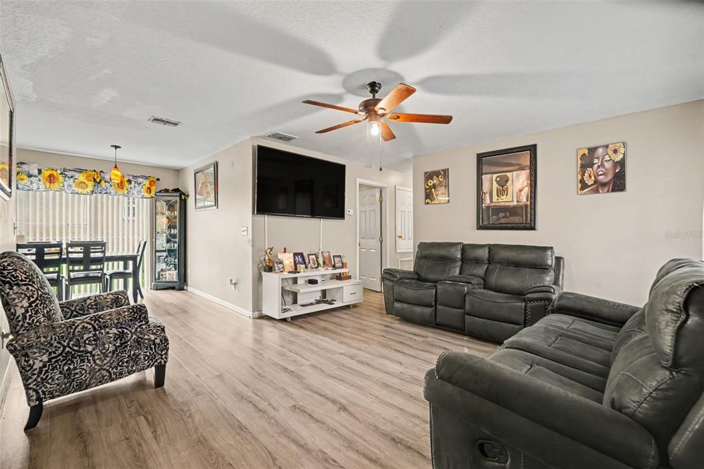 A living room features light wood-look flooring, a ceiling fan, and dark leather furniture — 38638 PATTI LANE, DADE CITY, FL