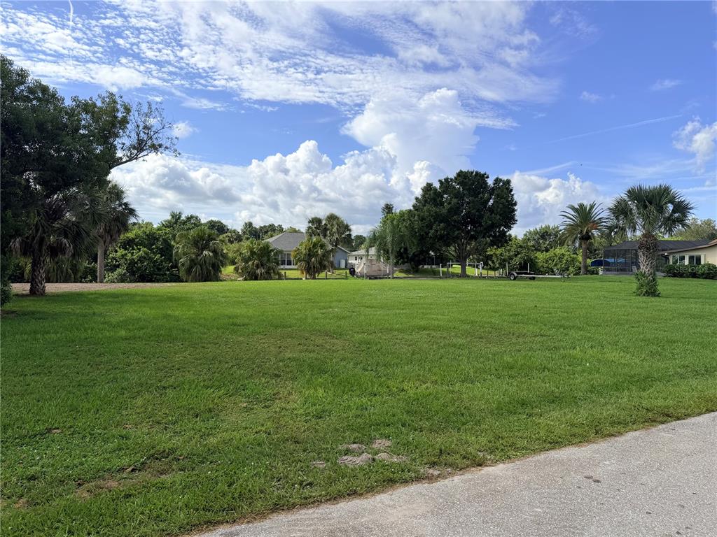 A large, grassy vacant lot features scattered trees under a blue sky with white clouds — 2036 RIVER BASIN TERRACE, PUNTA GORDA, FL