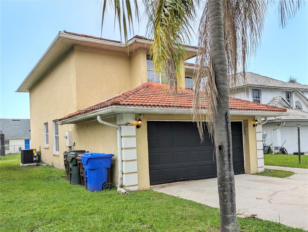 A two-story yellow house features a two-car garage, a tiled roof, and three trash bins — 423 WATERFORD WAY, KISSIMMEE, FL