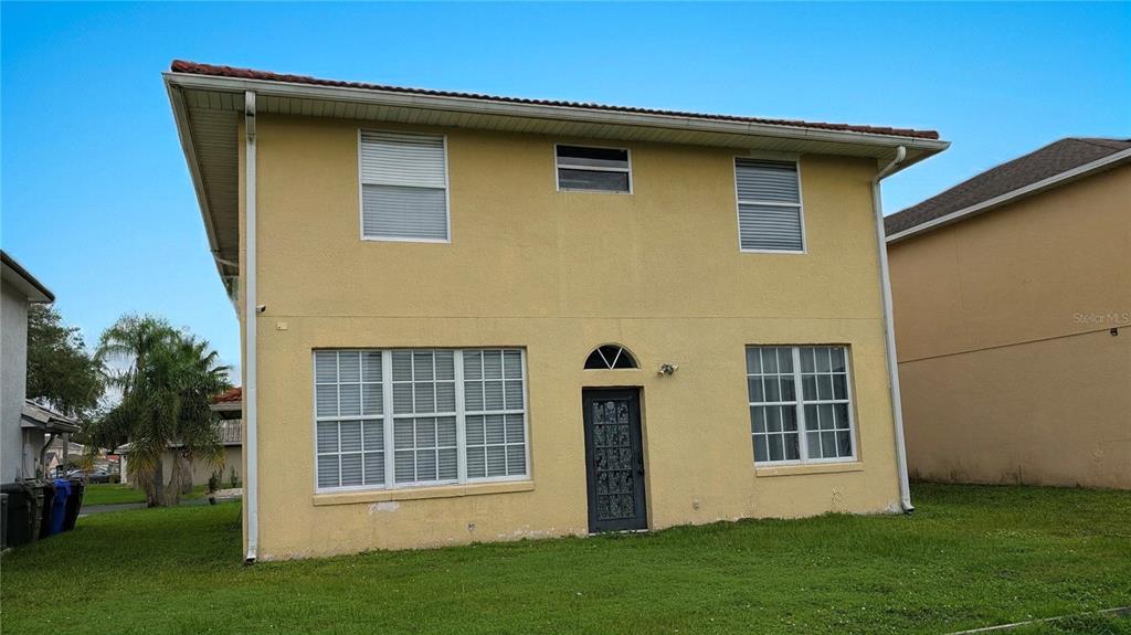 The exterior rear view of a two-story yellow stucco house with a dark door — 423 WATERFORD WAY, KISSIMMEE, FL