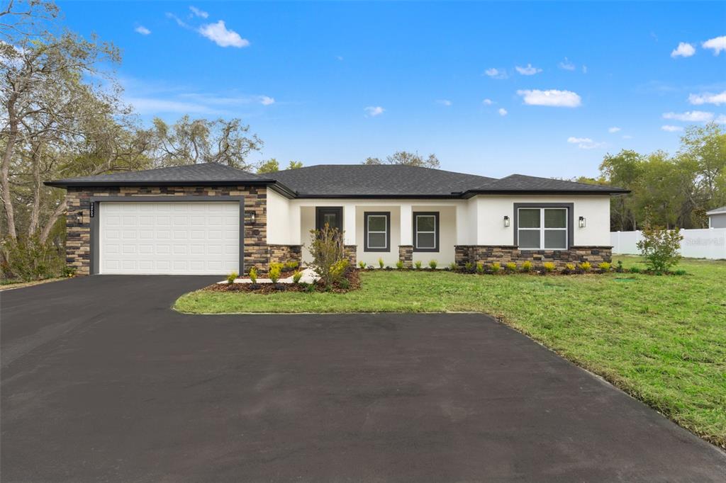 A single-story house with a white stucco facade, stone accents, and a two-car garage — 14905 PEACE BOULEVARD, SPRING HILL, FL