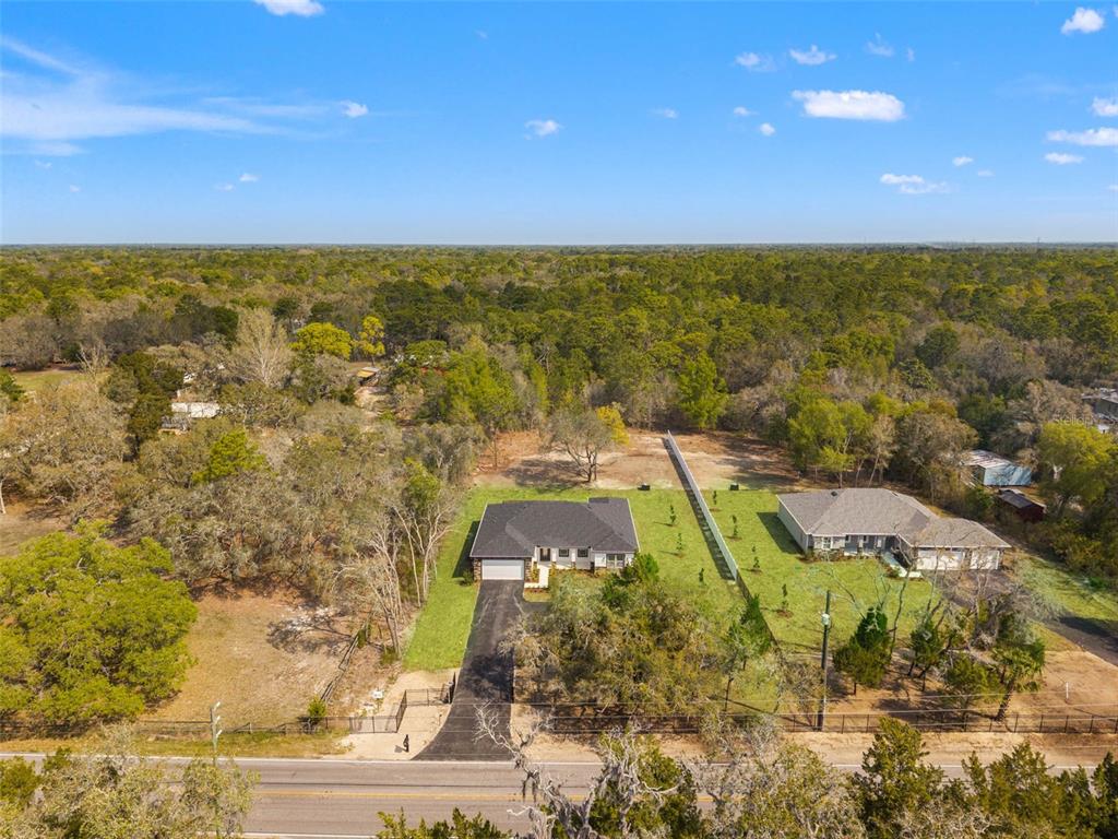 An aerial view shows two houses with driveways and fenced yards surrounded by dense forest — 14905 PEACE BOULEVARD, SPRING HILL, FL