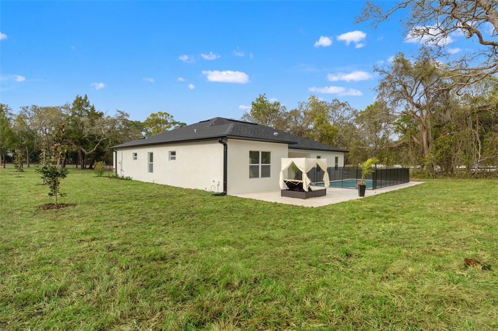 The exterior of a white house features a backyard pool, patio, and surrounding grassy lawn — 14905 PEACE BOULEVARD, SPRING HILL, FL