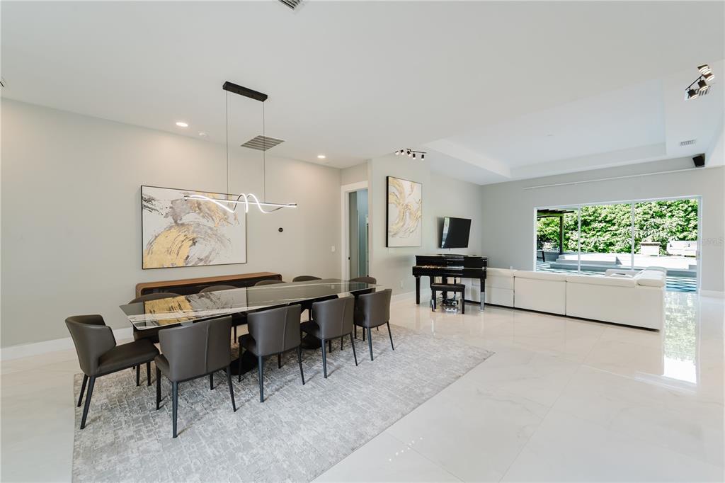 A modern open-concept dining and living area features a glass table, piano, and white sofa — 1361 WHITNEY ISLES DRIVE, WINDERMERE, FL