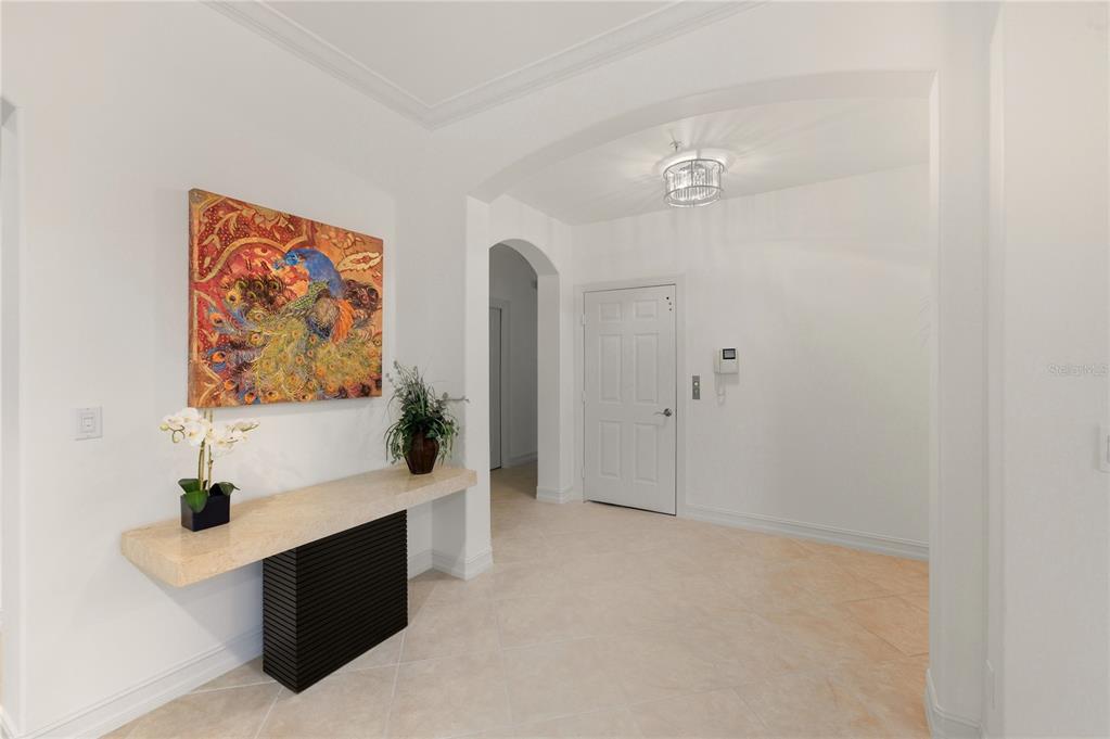A bright entryway features a stone console table, a peacock painting, and tile flooring — 2843 TIBURON BOULEVARD E UNIT 7-102, NAPLES, FL