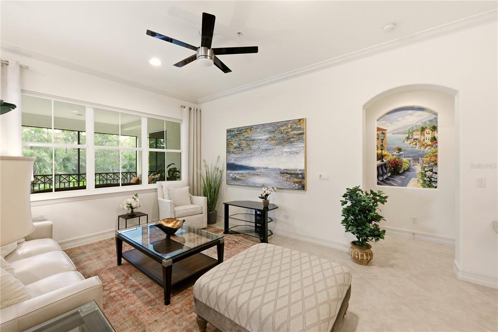 A bright living room features a white sofa, glass coffee table, and an arched wall mural — 2843 TIBURON BOULEVARD E UNIT 7-102, NAPLES, FL