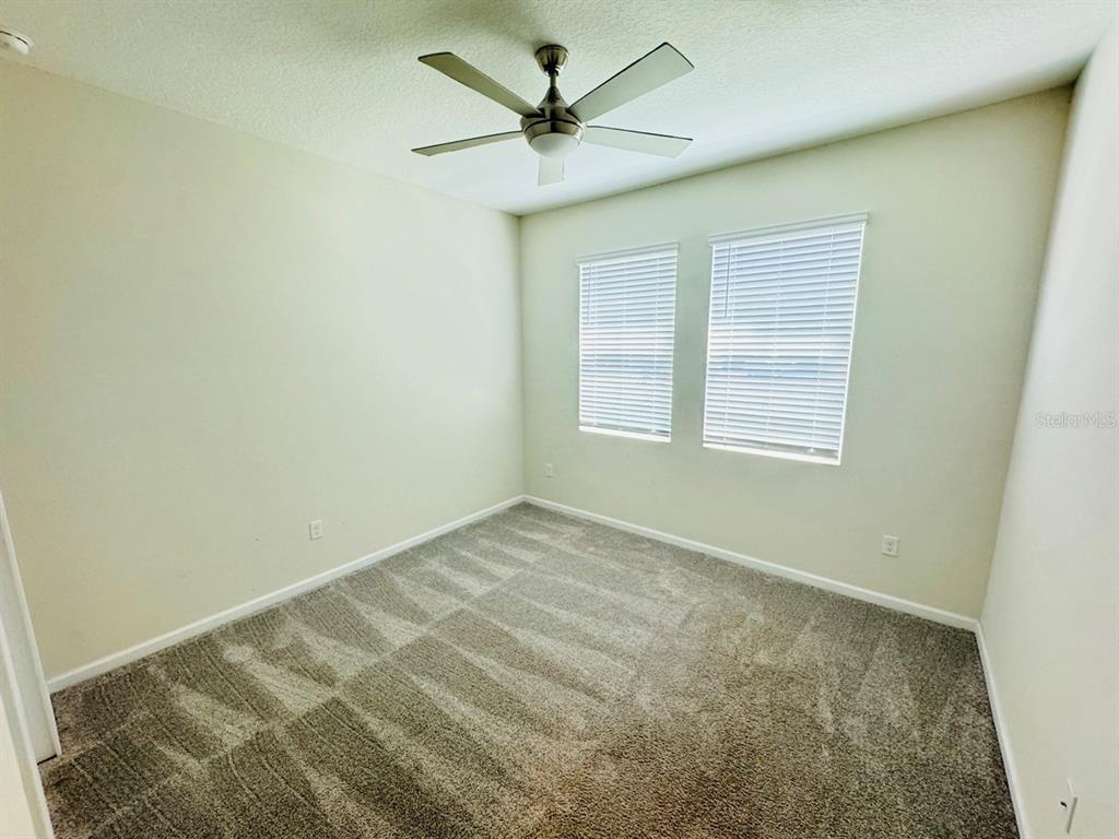 An empty bedroom features beige walls, gray carpet, a ceiling fan, and two windows — 1711 LAKE SIMS PARKWAY, OCOEE, FL