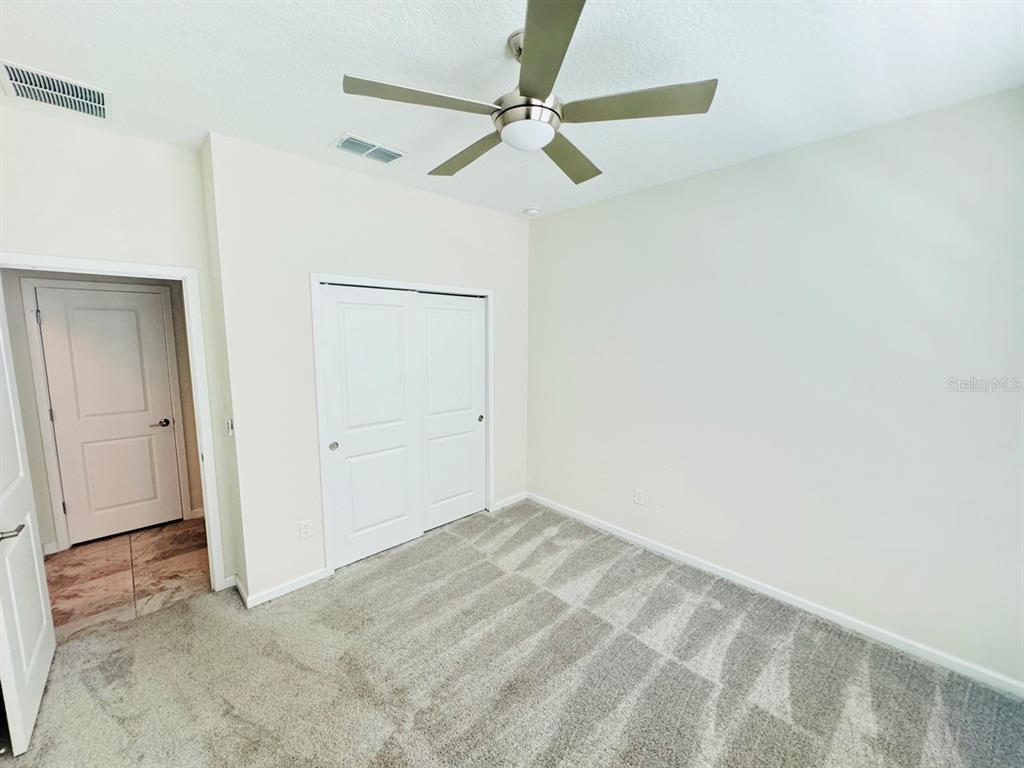 A bedroom with beige walls, gray carpet, a ceiling fan, and white closet doors — 1711 LAKE SIMS PARKWAY, OCOEE, FL