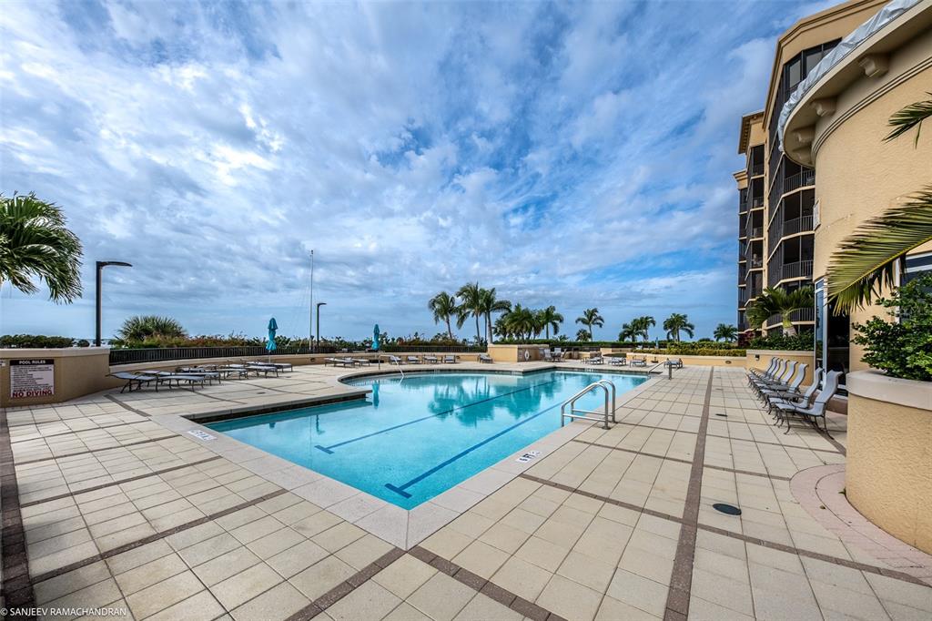 An outdoor swimming pool with lounge chairs on a paved deck beside a multi-story building — 3313 SUNSET KEY CIRCLE UNIT 403, PUNTA GORDA, FL