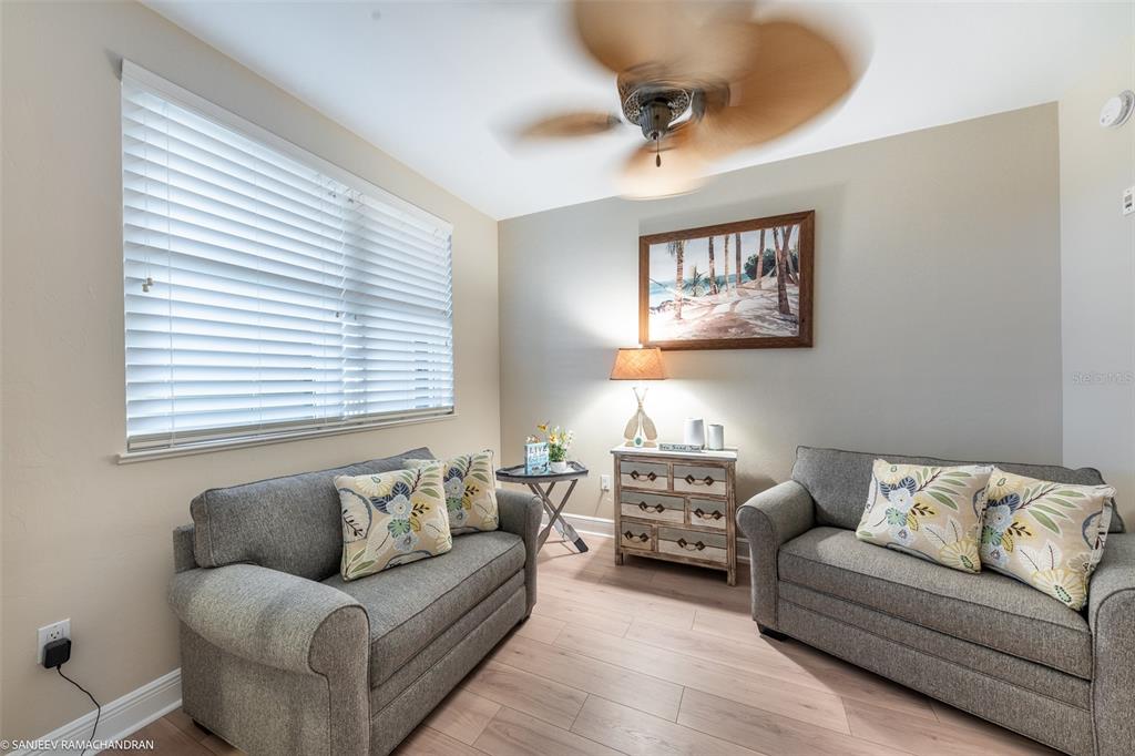 A living room features two gray sofas, wood-look flooring, a ceiling fan, and wall art — 3313 SUNSET KEY CIRCLE UNIT 403, PUNTA GORDA, FL