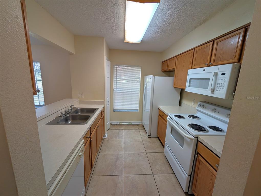 A galley kitchen features oak cabinets, white appliances, a double sink, and tiled flooring — 4053 DOLPHIN DRIVE, TAMPA, FL