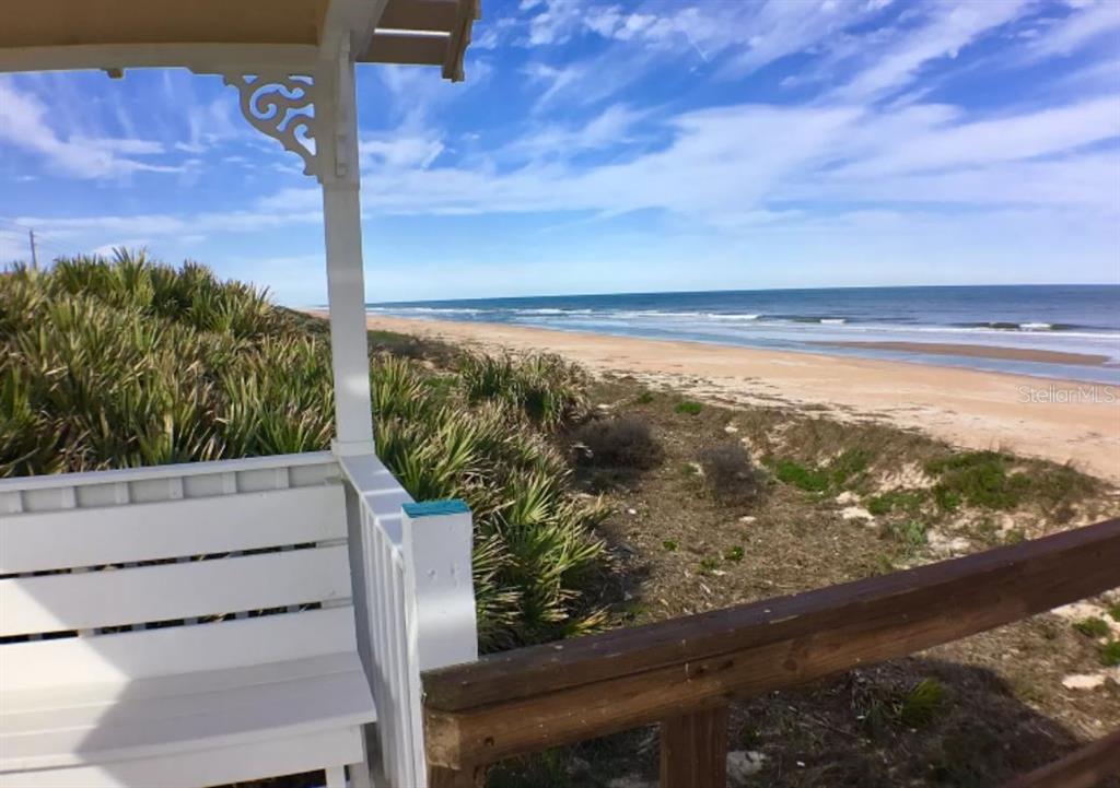 A view of a sandy beach and ocean from a white wooden porch deck — 148 COQUINA KEY DRIVE, ORMOND BEACH, FL