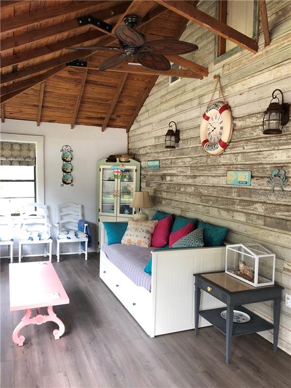 A sunroom features a daybed, a pink coffee table, and wood-paneled walls with nautical decor — 1302 2ND AVENUE E, BRADENTON, FL