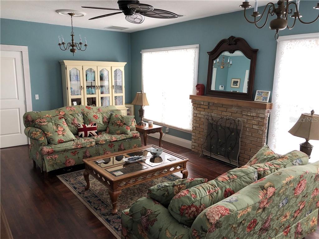 A living room features floral sofas, a brick fireplace, and blue walls with wood flooring — 1302 2ND AVENUE E, BRADENTON, FL