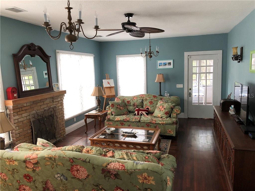 A living room features blue walls, floral sofas, a brick fireplace, and dark wood flooring — 1302 2ND AVENUE E, BRADENTON, FL