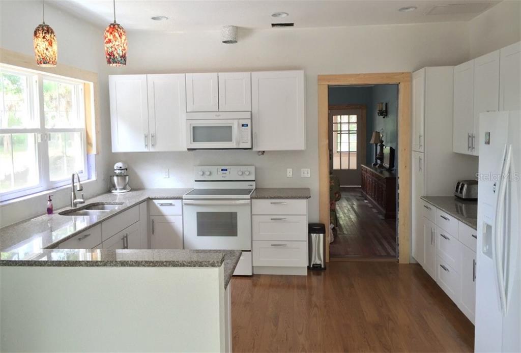 A kitchen with white cabinets, granite countertops, stainless steel appliances, and wood flooring — 1302 2ND AVENUE E, BRADENTON, FL