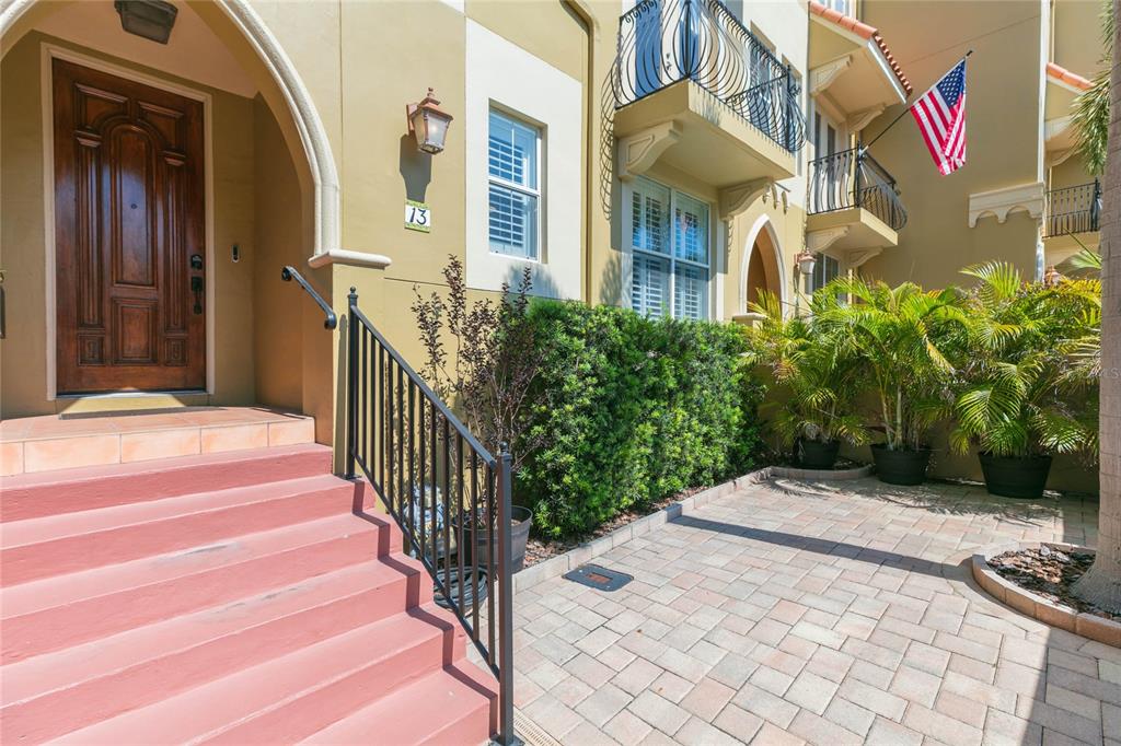 A tan townhouse exterior features a wooden front door, pink steps, and a paved patio — 114 E DAVIS BOULEVARD UNIT 13, TAMPA, FL