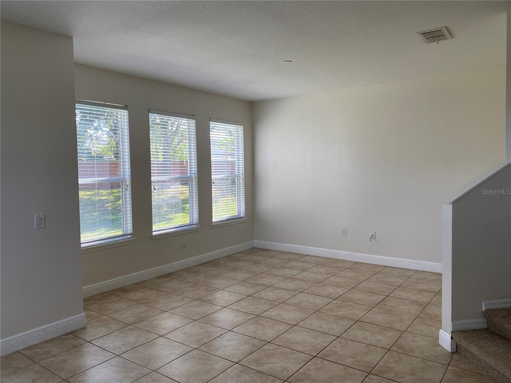 An empty room with beige tile flooring, three windows with blinds, and a staircase — 1903 ESTANCIA CIRCLE UNIT 1903, KISSIMMEE, FL
