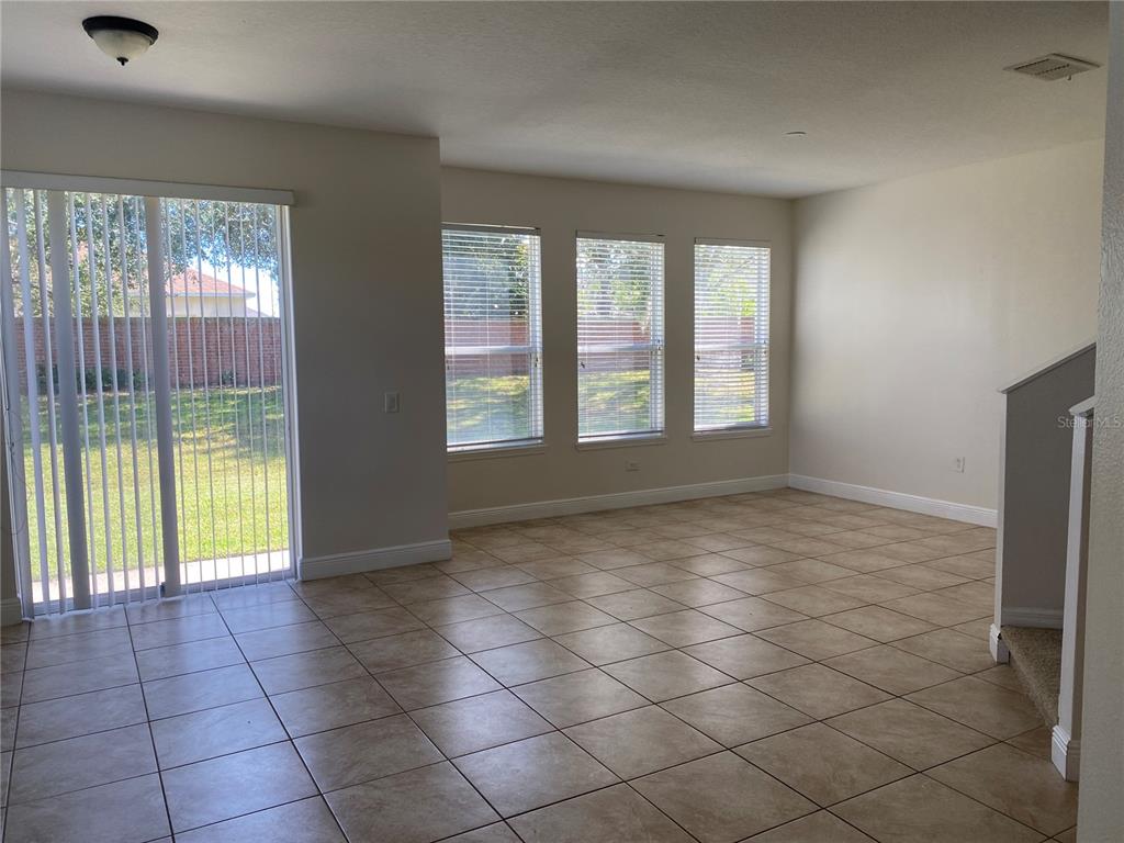 An empty room features beige tile flooring, three windows, and a sliding glass door — 1903 ESTANCIA CIRCLE UNIT 1903, KISSIMMEE, FL