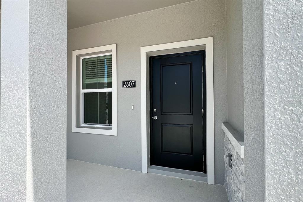 A black front door and a single window are set into a gray stucco exterior wall — 2607 SKYLINE LOOP, KISSIMMEE, FL
