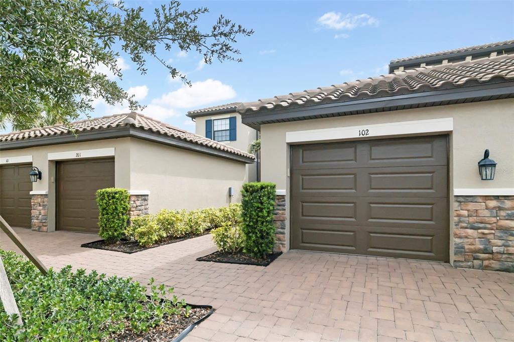 The exterior of two adjacent residential buildings features brown garage doors and stone veneer accents — 13828 MESSINA LOOP UNIT 102, BRADENTON, FL