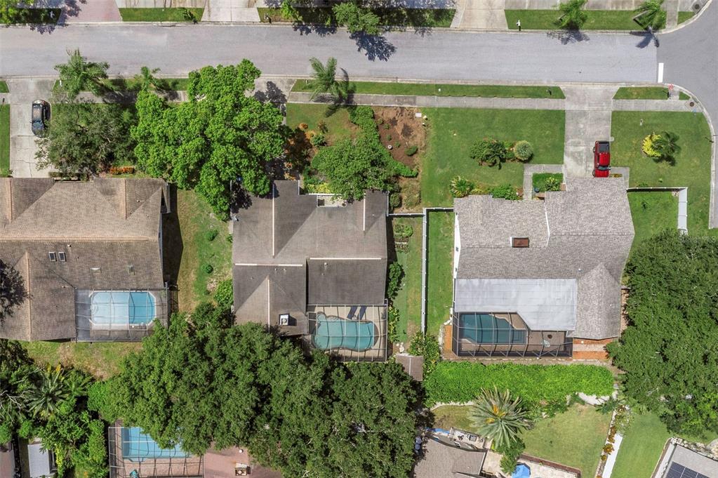 An aerial view shows three suburban houses with swimming pools and surrounding trees and lawns — 1620 COUNTRY LANE, DUNEDIN, FL