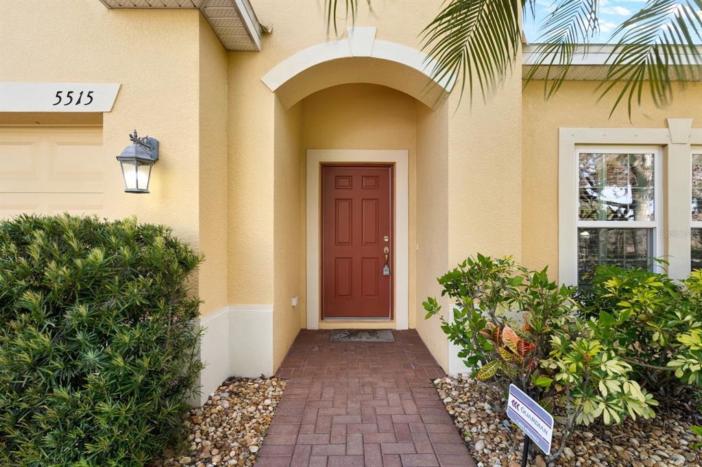 The exterior of a home features a red front door, a brick walkway, and landscaping — 5515 74TH PLACE E, ELLENTON, FL