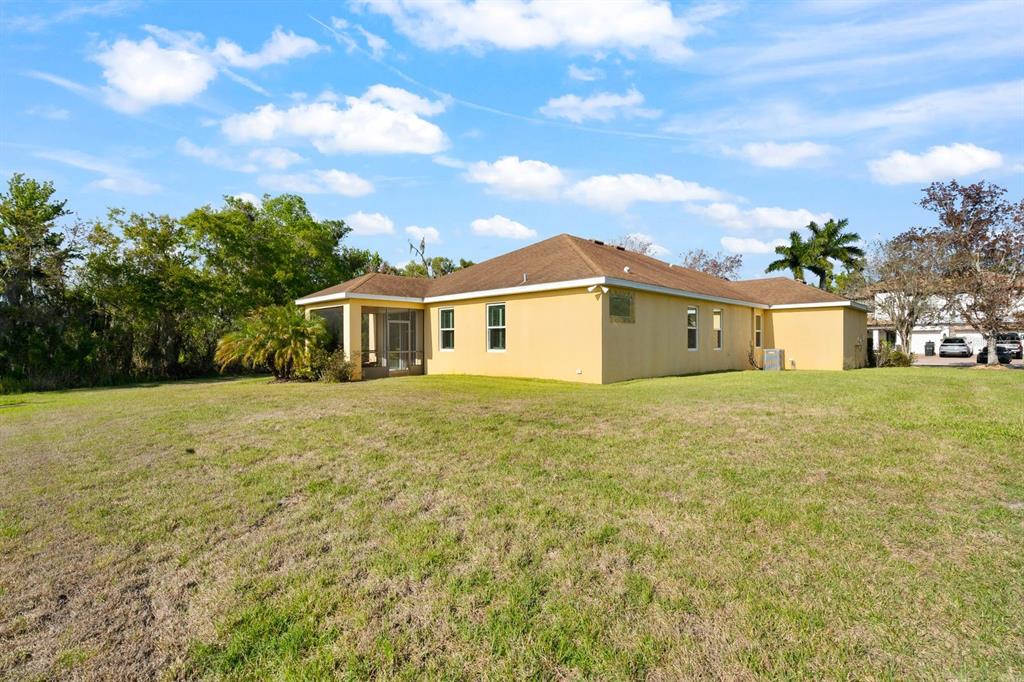 The rear exterior of a yellow, single-story house features a screened-in patio and lawn — 5515 74TH PLACE E, ELLENTON, FL