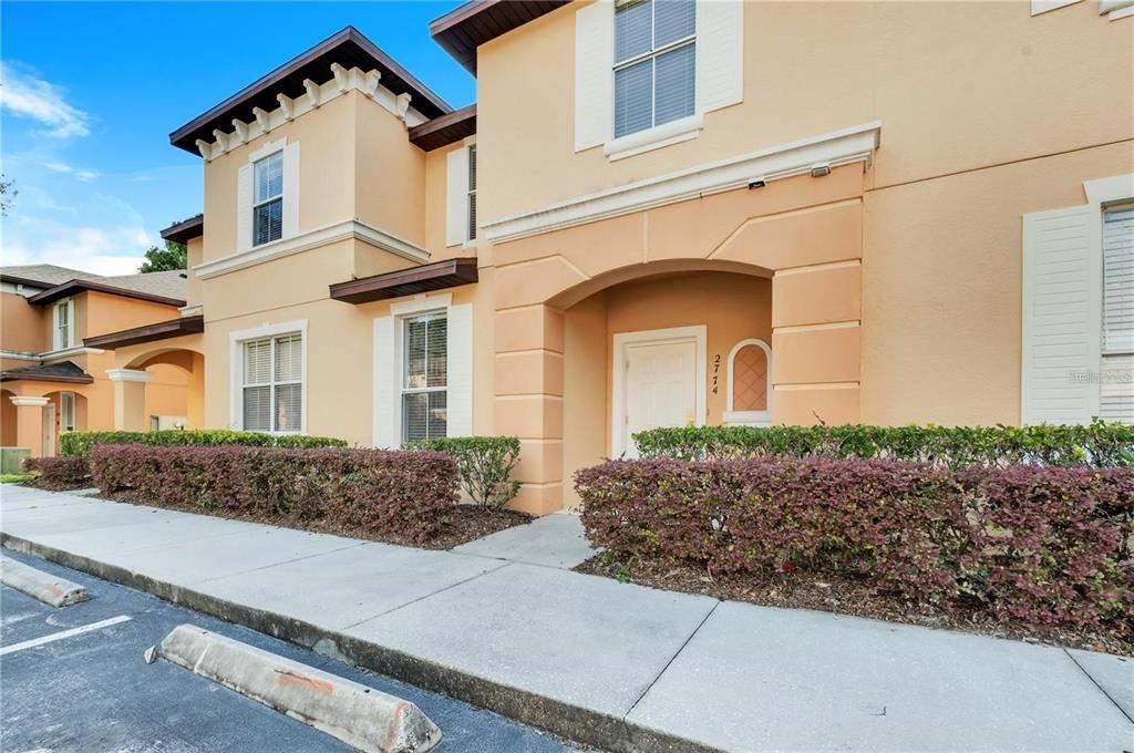 A two-story peach-colored townhouse exterior features a covered entryway, white shutters, and a front hedge — 2774 CORVETTE LANE, KISSIMMEE, FL