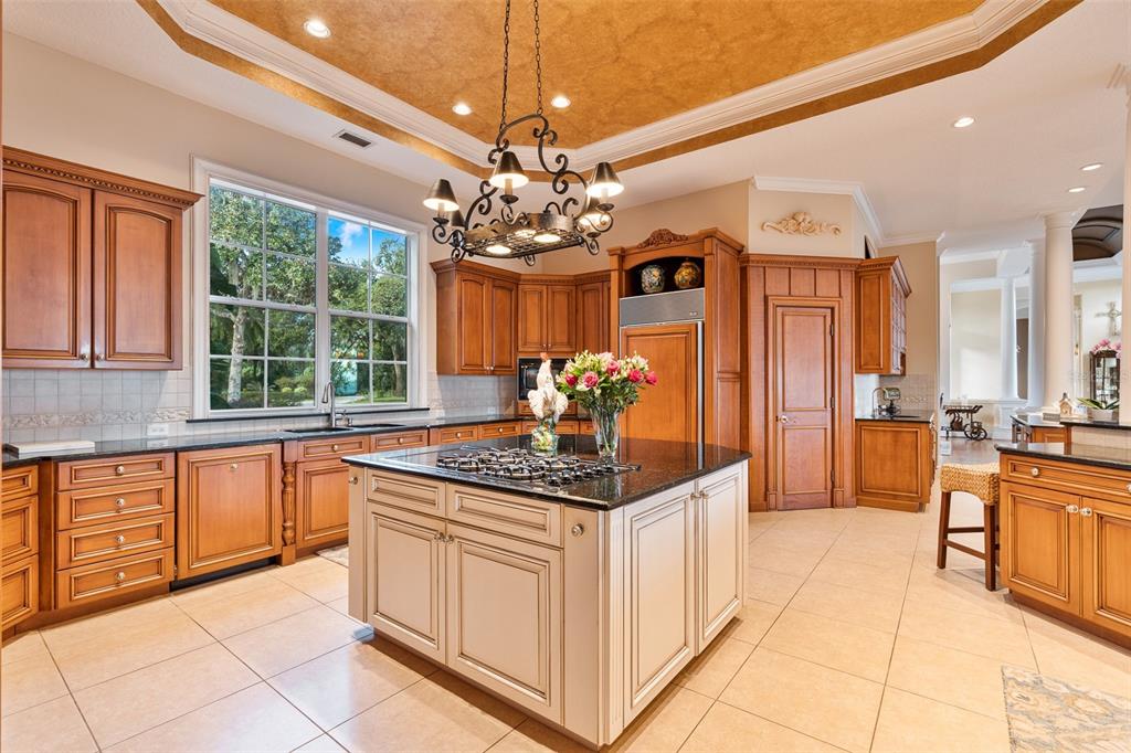 A kitchen features wood cabinetry, a central island with a gas cooktop, and tile flooring — 30215 REDTREE DRIVE, LEESBURG, FL