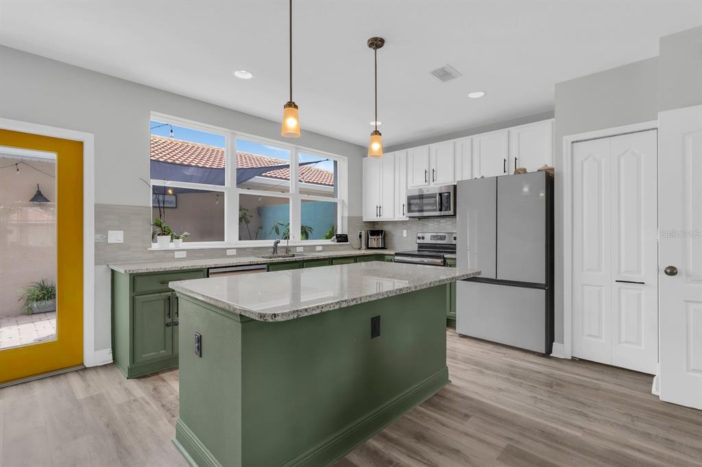 A kitchen features green base cabinets, a granite-topped island, white upper cabinets, and a yellow door — 3113 VIA OTERO DRIVE, KISSIMMEE, FL