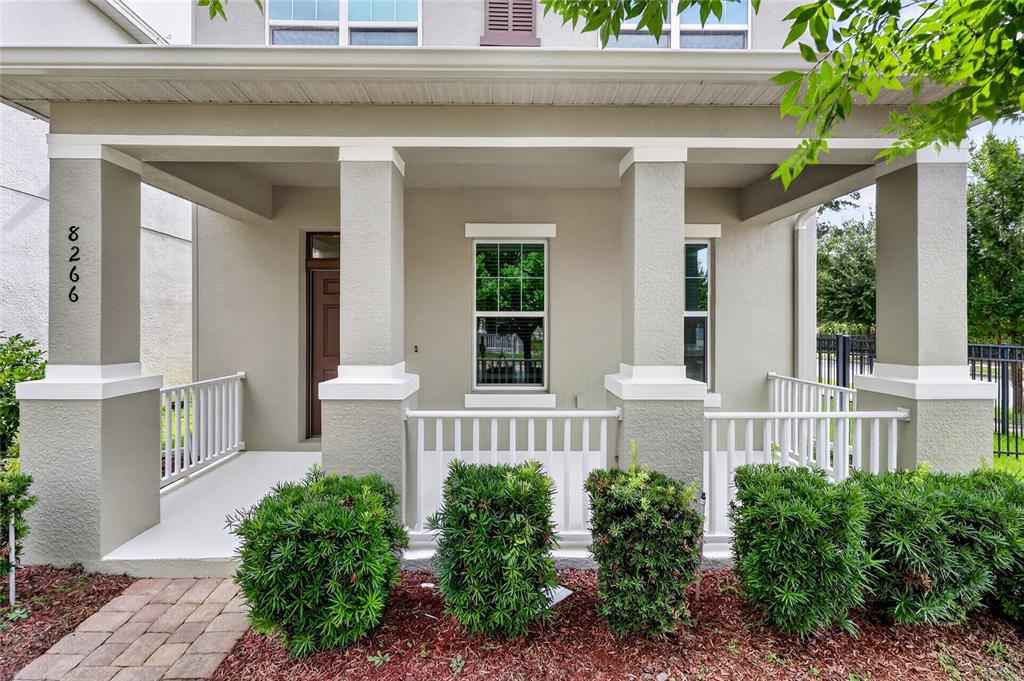 A front porch with white railings and columns sits before a house with beige siding — 8266 BRYCE CANYON AVENUE, WINDERMERE, FL