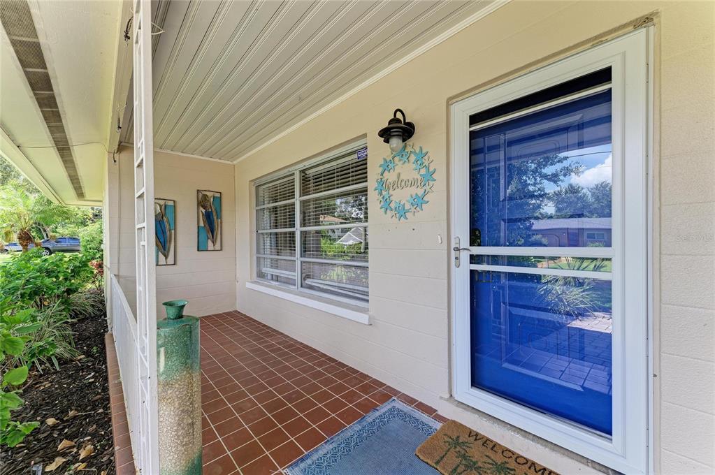 A covered front porch features tiled flooring, a blue storm door, and a welcome wreath — 1214 21ST STREET W, BRADENTON, FL