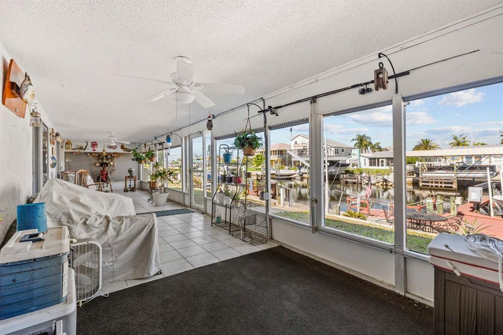 A screened-in porch with tiled flooring overlooks a canal with boat docks and houses — 15639 BERTRAM DRIVE, HUDSON, FL