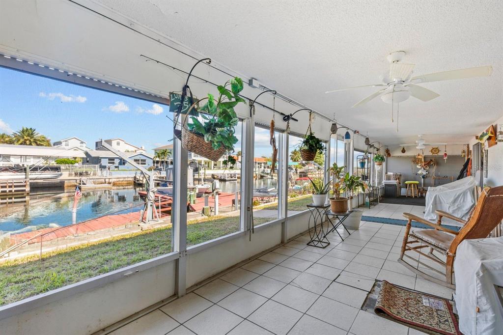 A screened-in porch with tiled flooring overlooks a canal with boat docks and houses — 15639 BERTRAM DRIVE, HUDSON, FL
