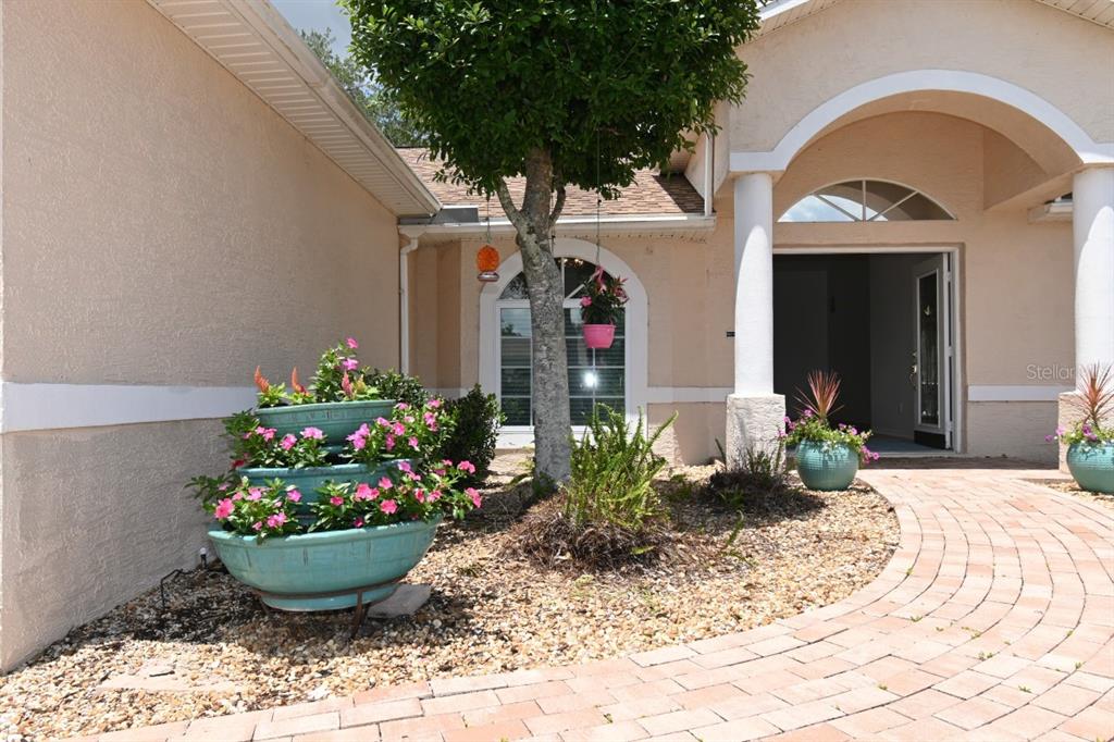 A paved walkway leads to the front entrance of a house with a tiered planter — 12125 KNOTTY PINE LOOP, SAN ANTONIO, FL