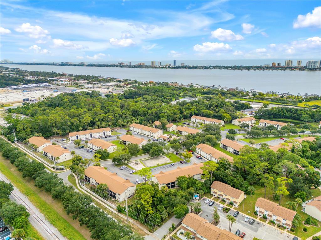 An aerial view shows a multi-building apartment complex surrounded by trees near a large body of water — 430 BANANA CAY DRIVE UNIT A, SOUTH DAYTONA, FL