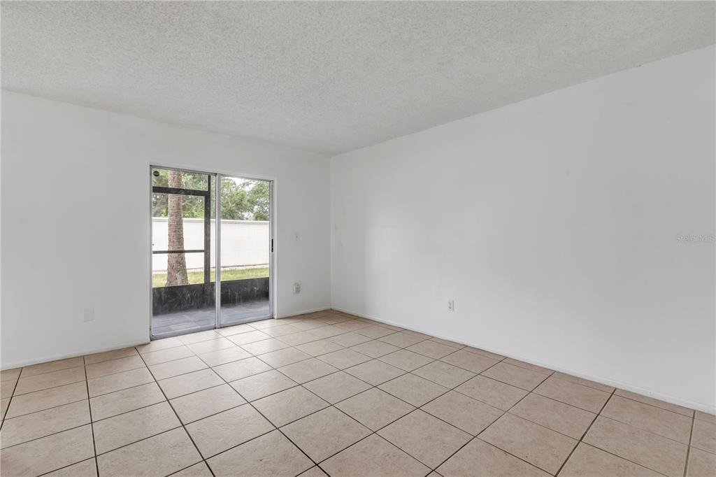 An empty room with beige tile flooring, white walls, and a sliding glass door — 430 BANANA CAY DRIVE UNIT A, SOUTH DAYTONA, FL