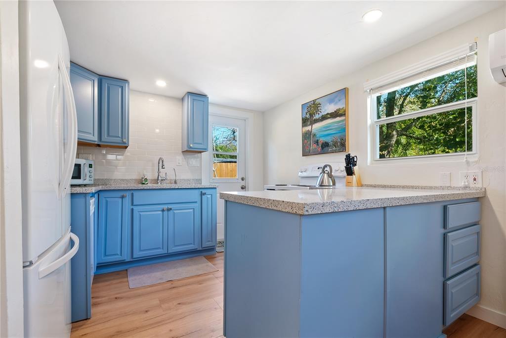 A kitchen features blue cabinets, granite countertops, a white subway tile backsplash, and wood flooring — 2311 WALDEMERE STREET UNIT B, SARASOTA, FL