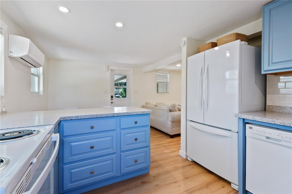 A kitchen features blue cabinets, white appliances, granite countertops, and a view into the living room — 2311 WALDEMERE STREET UNIT B, SARASOTA, FL