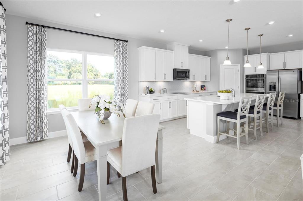 A bright kitchen and dining area featuring white cabinetry, a large island, and tile flooring — 443 HAMMOCK OAKS BOULEVARD, LADY LAKE, FL
