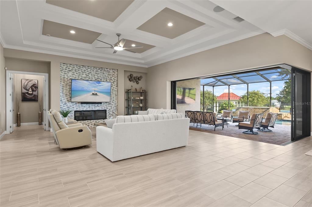 A spacious living room features a coffered ceiling, fireplace, and large sliding doors opening to a patio — 209 PINE LILLY COURT, LAKE ALFRED, FL