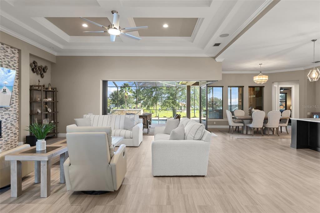 A living room with light tile floors, a tray ceiling, and sliding doors opening to a pool — 209 PINE LILLY COURT, LAKE ALFRED, FL