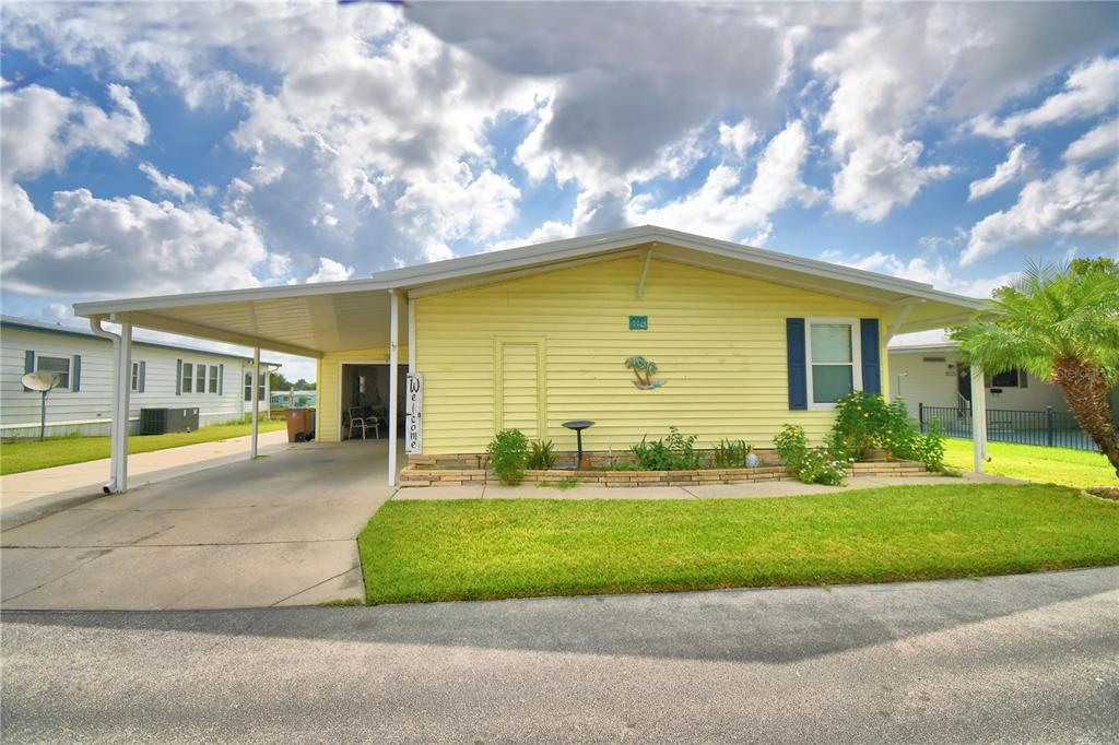 A yellow single-story mobile home features a carport, a front lawn, and a small garden — 2055 S FLORAL AVENUE UNIT 119, BARTOW, FL
